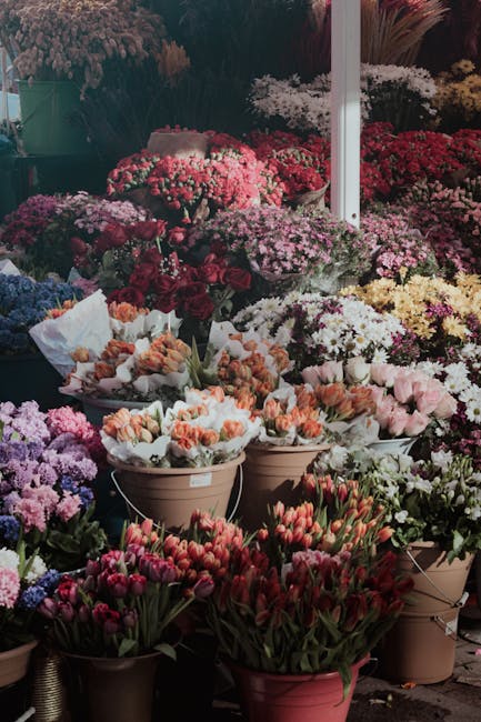 An extensive display of fresh flowers arranged in various pots and containers at a floral market stall. The arrangement includes a wide variety of blooms such as pink and white tulips, purple and pink