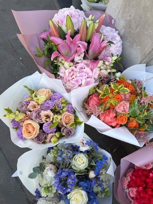 A collection of five flower bouquets arranged for delivery, featuring a variety of fresh blooms. The central bouquet showcases pink lilies, light pink hydrangeas, and lush green foliage, wrapped in la